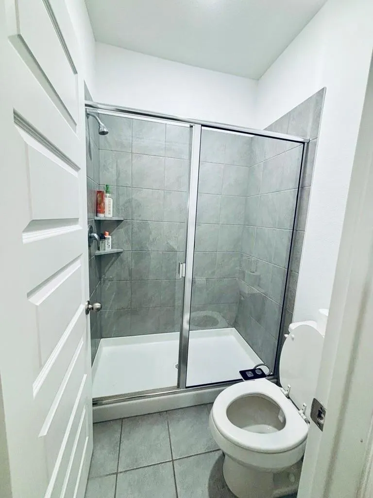 Enclosed shower with sliding glass doors, tiled walls, and a built-in corner shelf