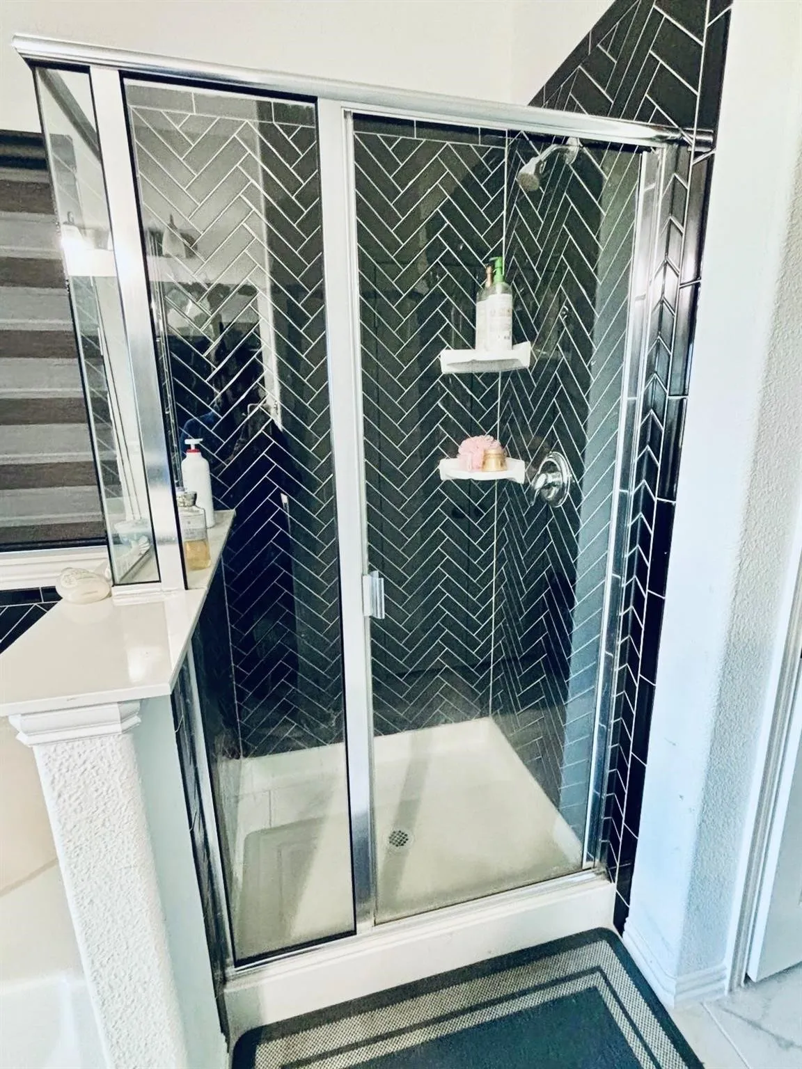 Shower enclosure with dark herringbone tile, chrome hardware, and glass sliding doors