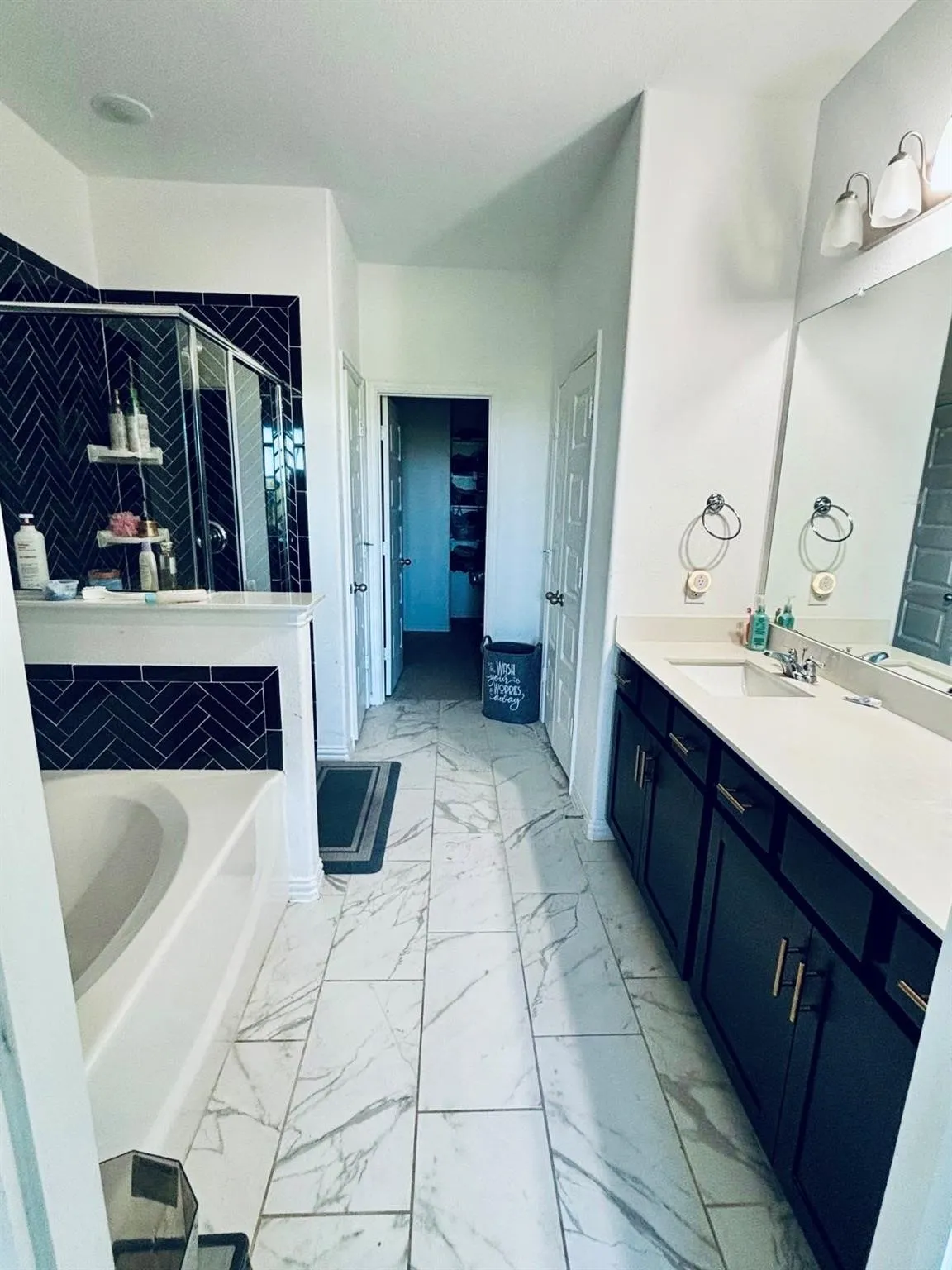 White tile flooring, a built-in bathtub, and a shower with dark herringbone tile