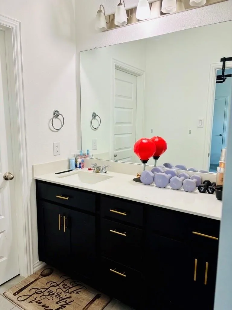 Vanity with black cabinetry, brass hardware, single basin sink, and a large wall-mounted mirror