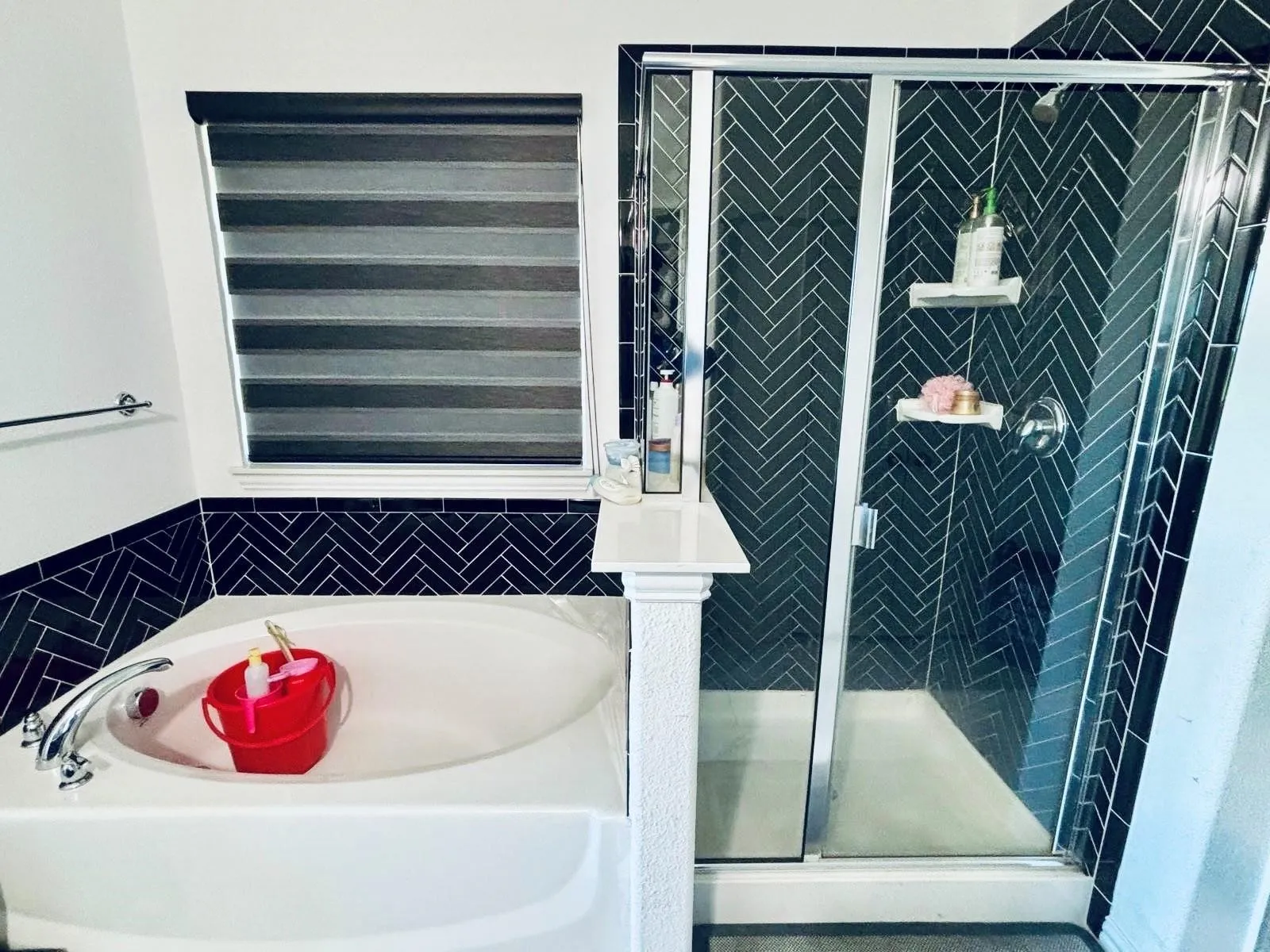 Built-in tub with chrome fixtures, glass-enclosed shower, and black herringbone tile detailing
