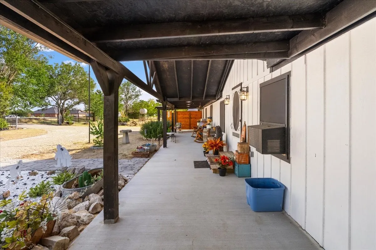 Covered concrete porch with dark wood beams, white vertical siding, and exterior wall sconces