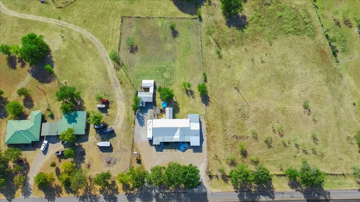 Expansive property featuring multiple structures, mature trees, and a paved road frontage