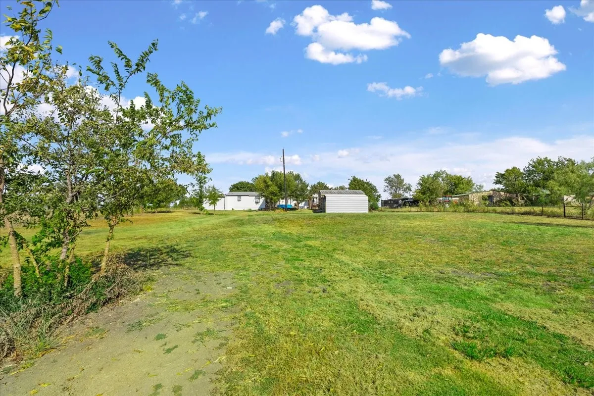 Expansive grassy area with scattered trees, a partial building structure, and a shed