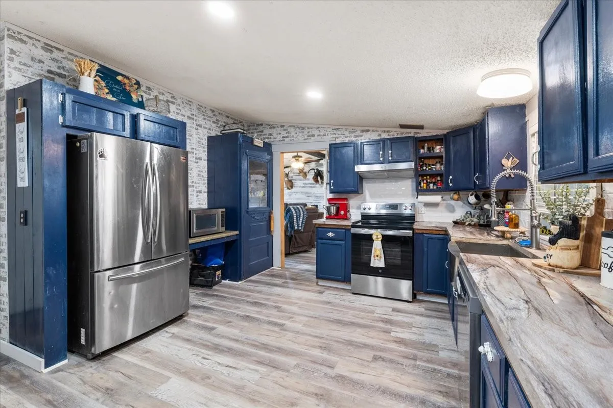 Contemporary kitchen featuring custom navy cabinetry, stainless steel French-door refrigerator, wood-finish flooring throughout, quartz countertops, and recessed ceiling lighting