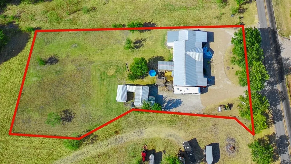 Expansive rural property featuring a main structure with a metal roof, an additional outbuilding, and a gravel driveway