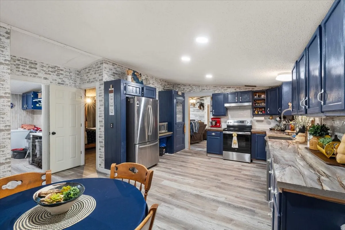Contemporary kitchen featuring custom navy cabinetry, stainless steel French-door refrigerator, wood-finish flooring throughout, quartz countertops, and recessed ceiling lighting