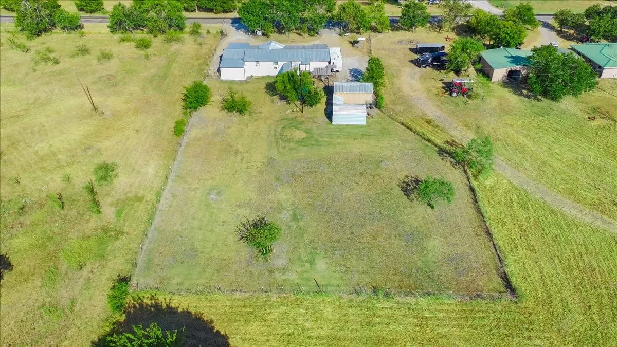 Expansive grassy acreage with perimeter fencing, featuring an unpaved entry, a white-sided residence, and multiple outbuildings