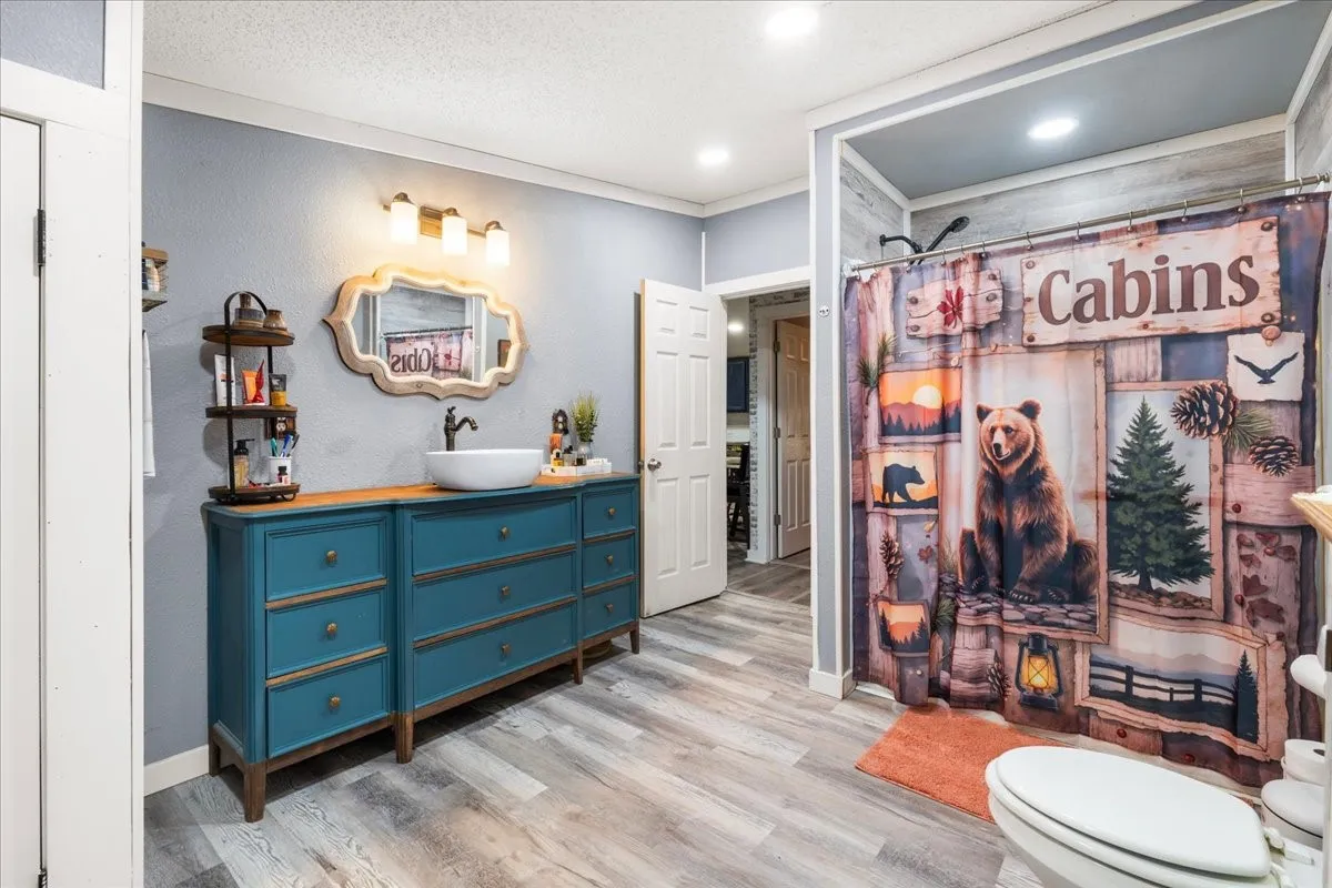Wood-finish flooring, accent wall with horizontal paneling, vanity with integrated basin, and wall-mounted light fixture