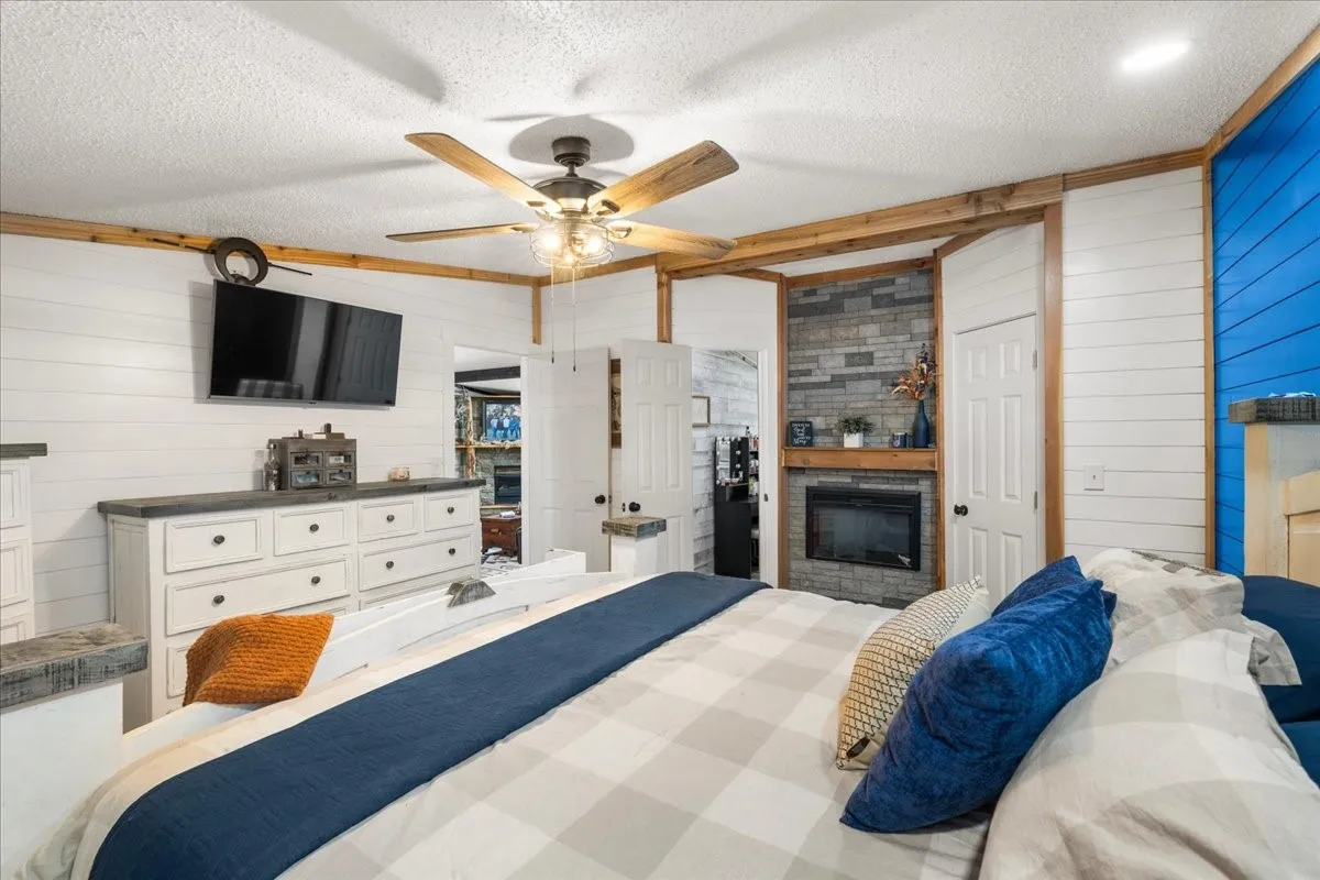 Shiplap wall paneling, ceiling fan, wood-finish trim, stone-clad fireplace with mantel, and built-in electric fireplace