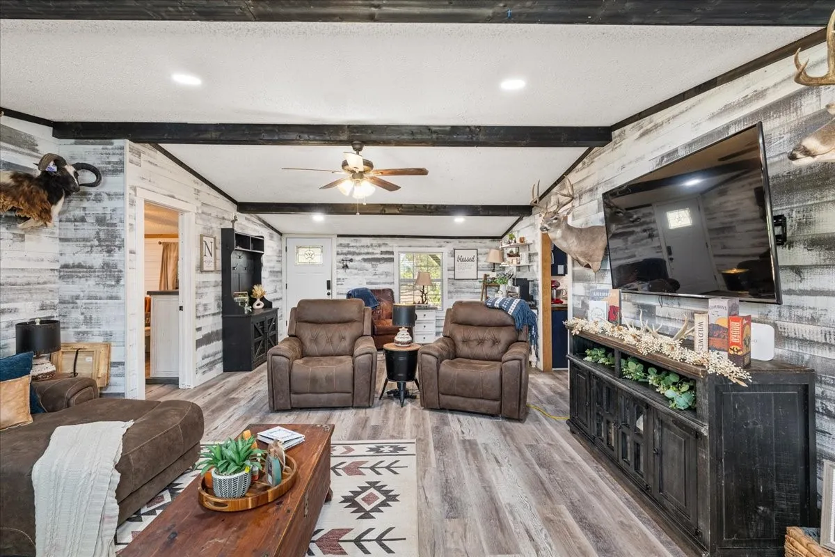 Wood-finish flooring, exposed ceiling beams, shiplap wall treatment, recessed lighting, and a built-in stone fireplace
