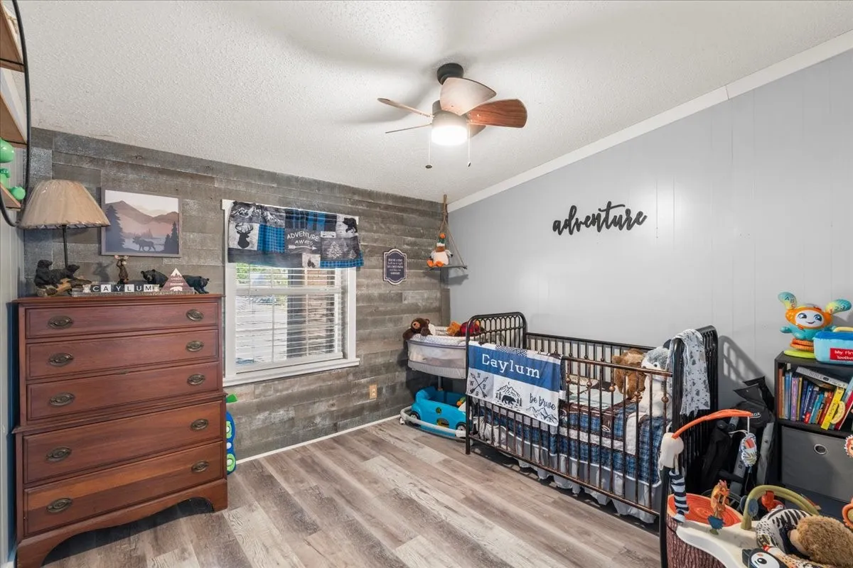 Wood-finish flooring, accent wall with horizontal paneling, ceiling fan, and white window blinds