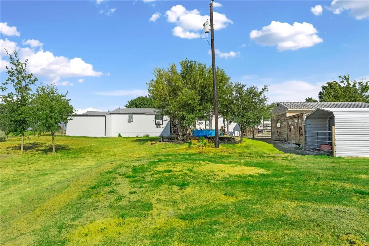 Expansive grassy terrain featuring mature trees, a detached storage structure, and a secondary metal-roofed structure