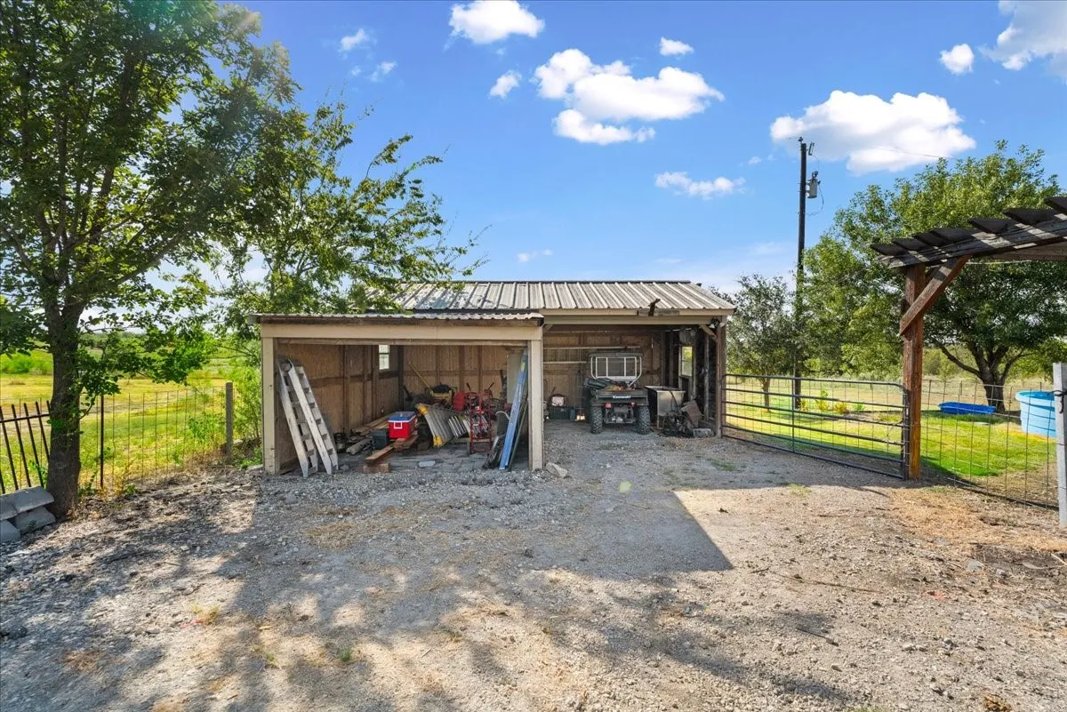 Covered storage structure with a corrugated metal roof and gravel ground cover