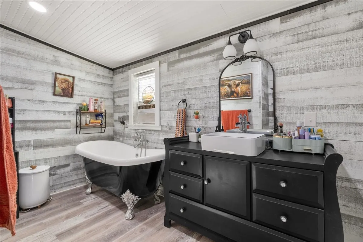 Freestanding clawfoot tub, wood-finish flooring, white shiplap ceiling, and light-tone wood-look wall paneling