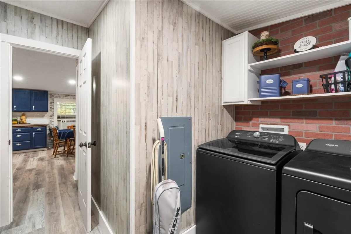 Laundry area featuring a textured accent wall, brick-patterned wall, white cabinetry, and open shelving