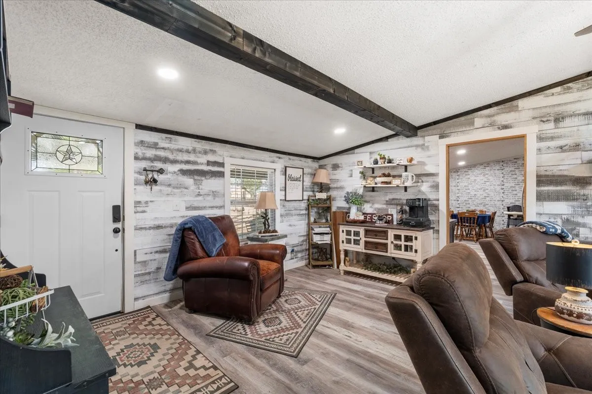 Wood-finish flooring, accent wall with shiplap-style paneling, exposed ceiling beams, and recessed lighting