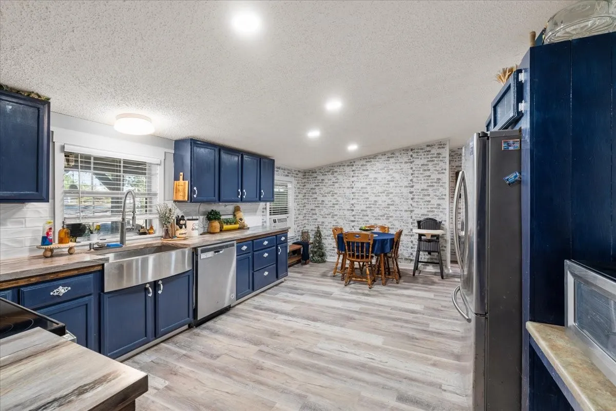 Kitchen featuring blue cabinetry, stainless steel appliances, wood-finish flooring, and a white subway tile backsplash