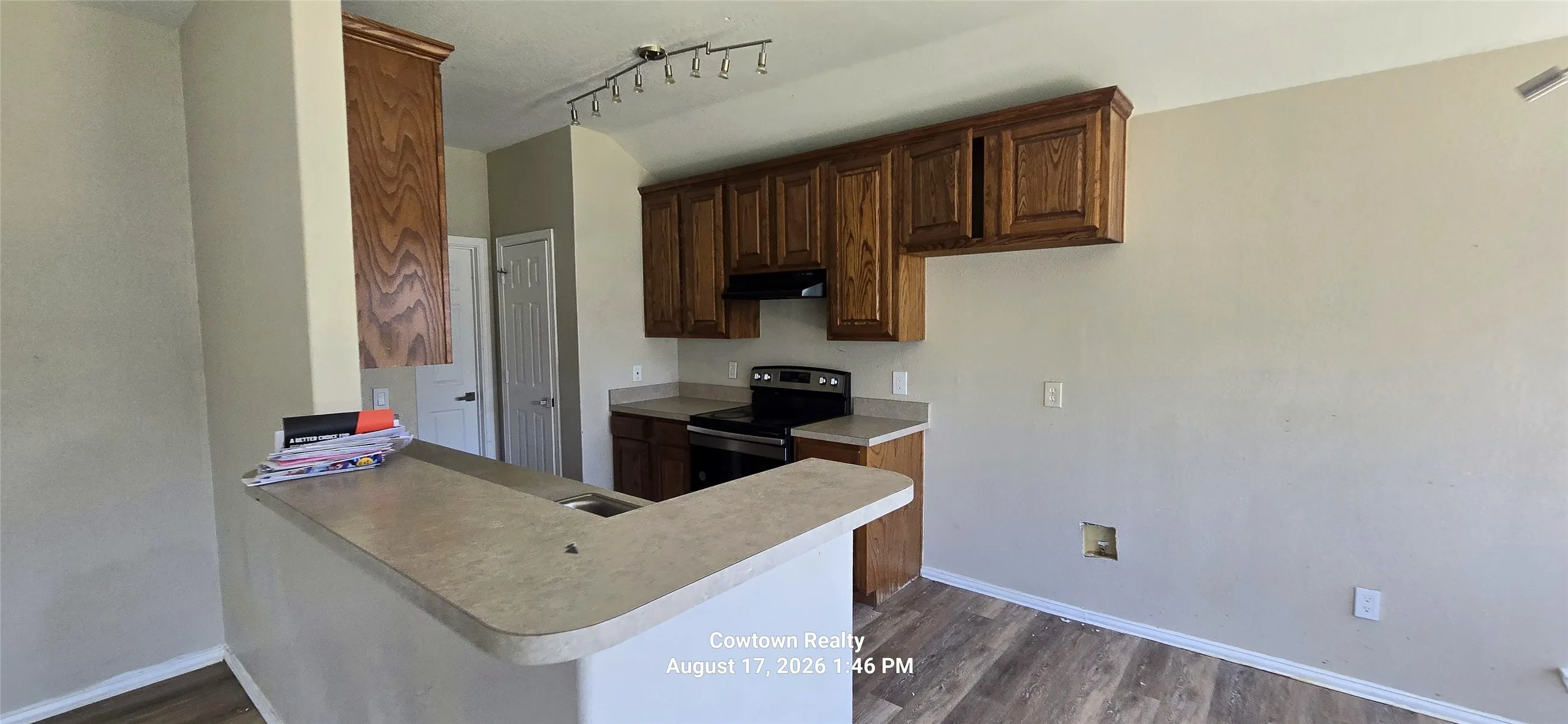 Kitchen featuring wood-finish flooring, wood cabinetry, built-in range, track lighting, and a breakfast bar