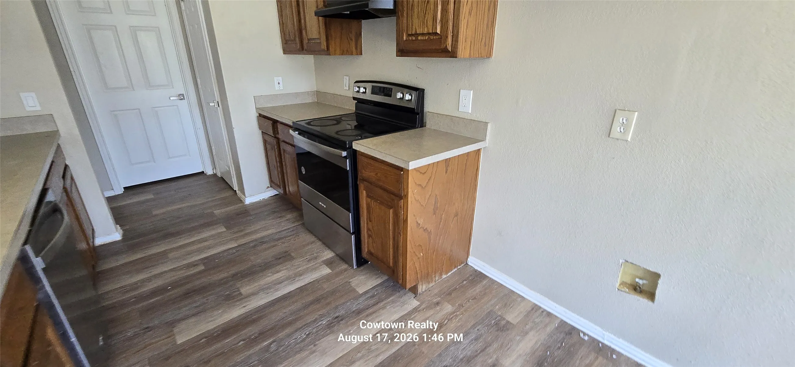 Wood-finish flooring, light-toned countertops, wood cabinetry, stainless steel range, and dishwasher
