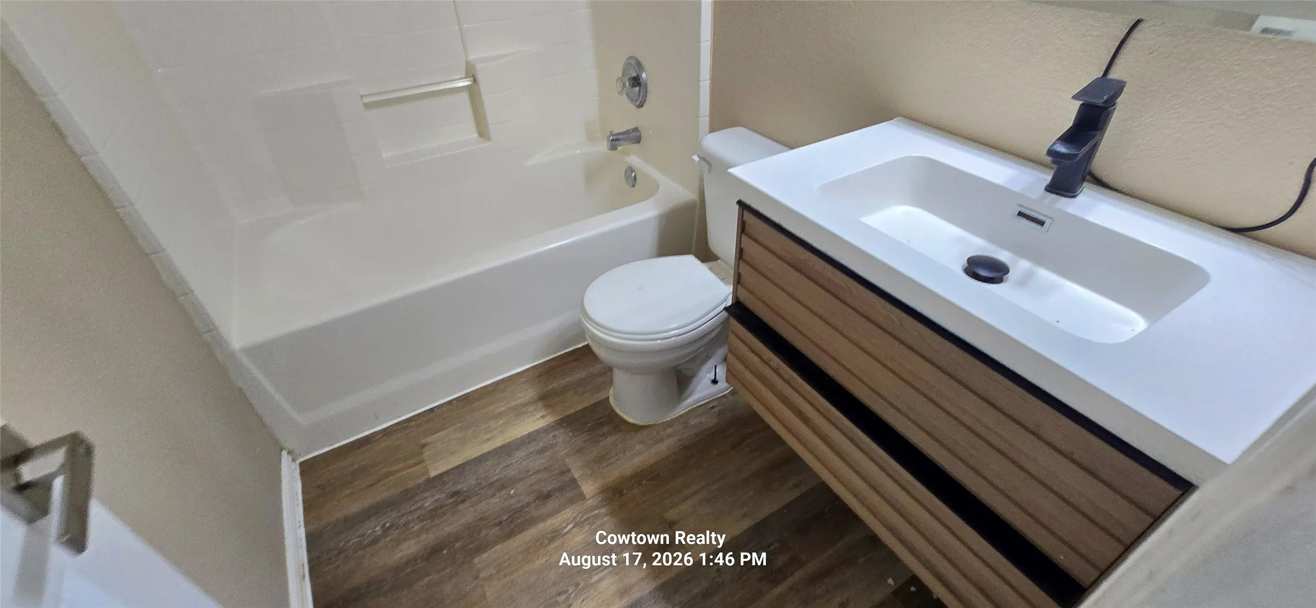 Wood-finish flooring with a white bathtub and integrated shower