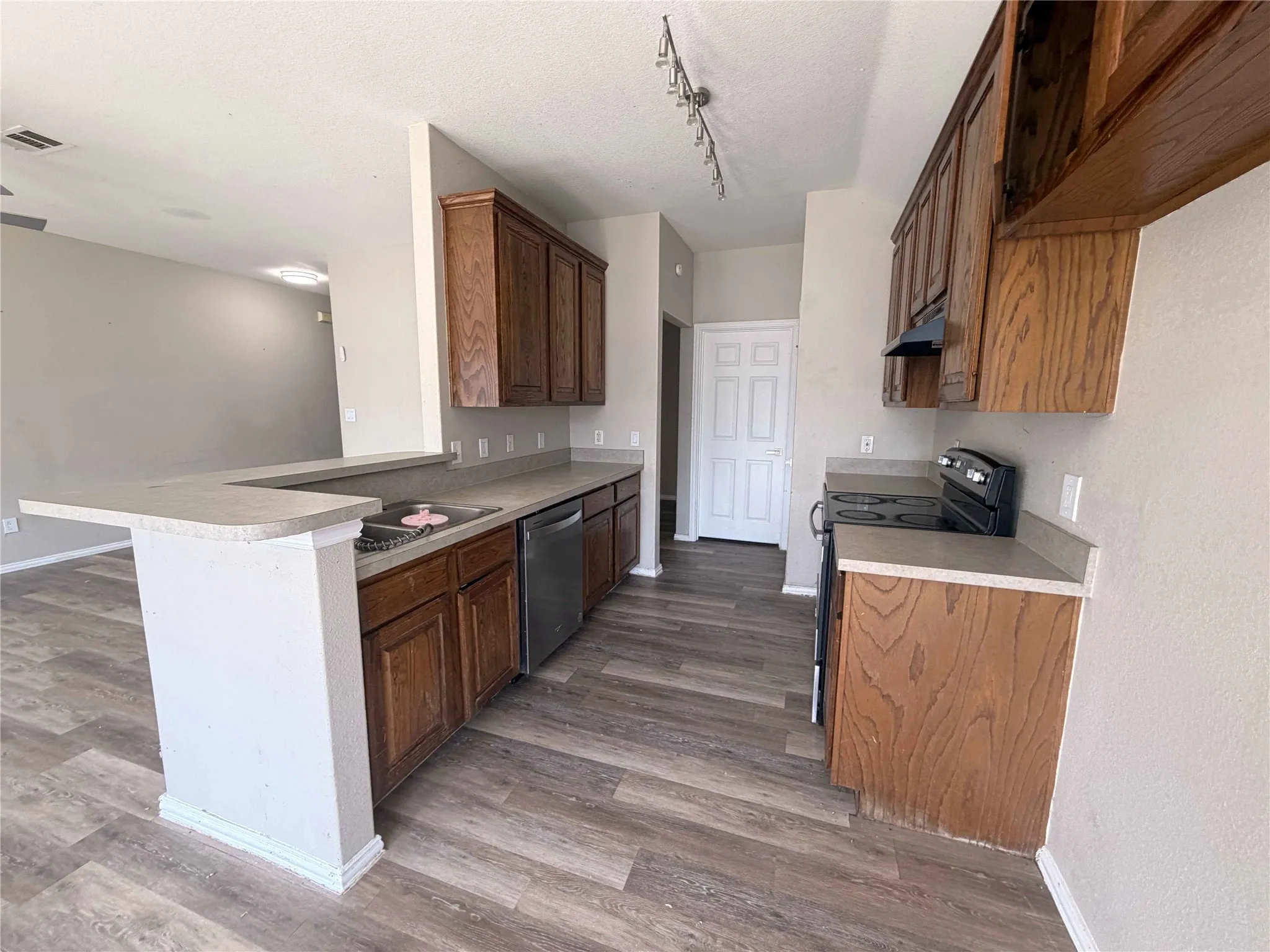 Kitchen featuring wood-finish flooring, wood cabinetry, stone-finish countertops, stainless steel dishwasher, and a built-in electric range
