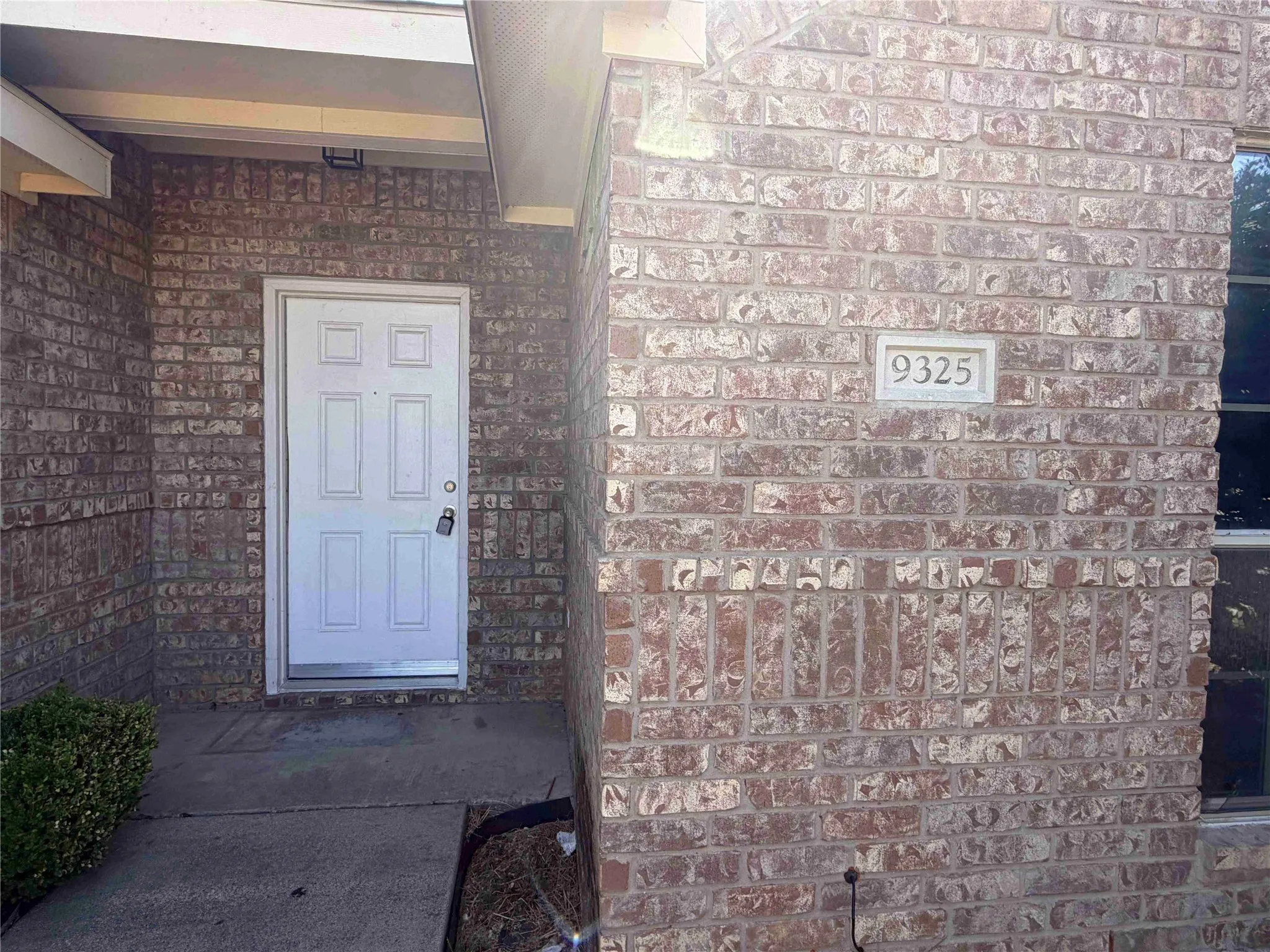 Brick exterior with a recessed entryway, featuring a paneled door, concrete pathway, and a visible address plaque