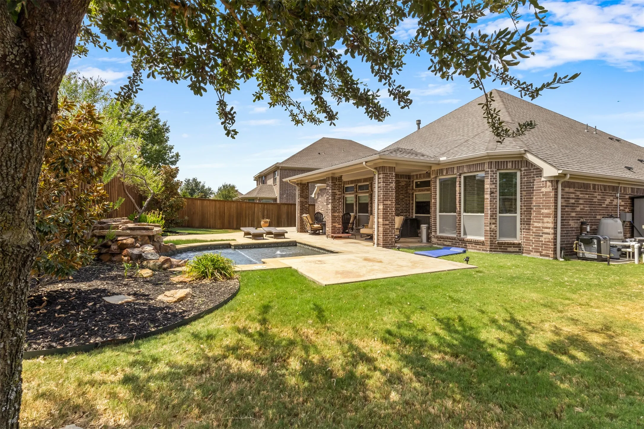 Expansive backyard featuring a manicured lawn, a swimming pool with a rock waterfall, and a concrete patio