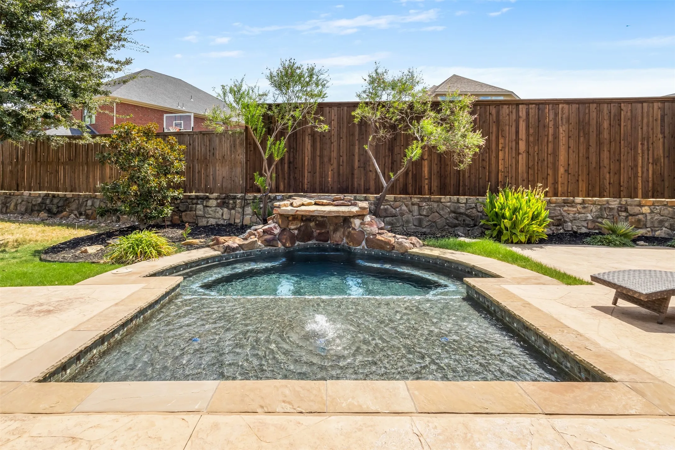 Pool with integrated spa, stone coping, natural stone waterfall feature, and surrounding patio