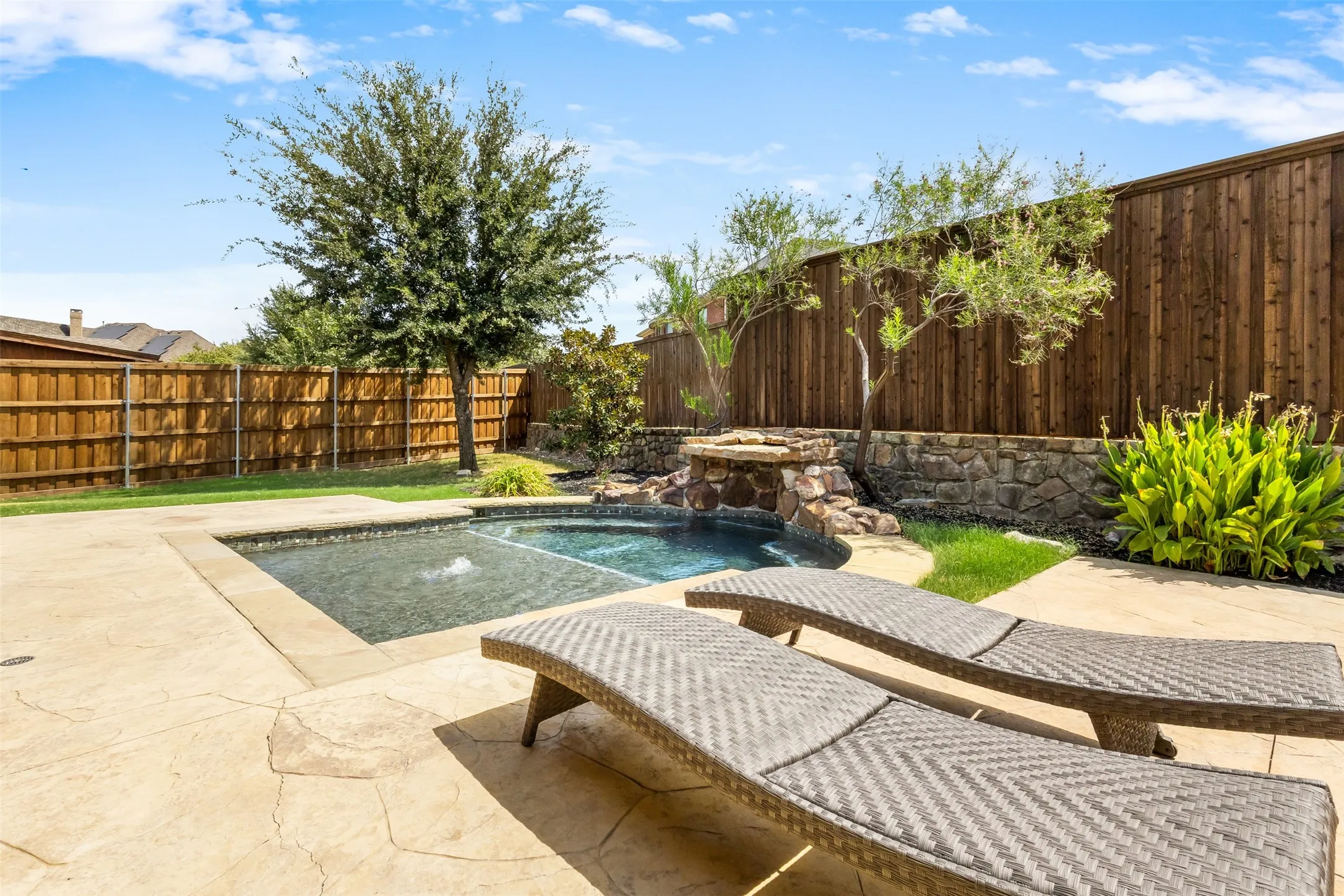 Private fenced backyard featuring a swimming pool, stone water feature, and stamped concrete patio