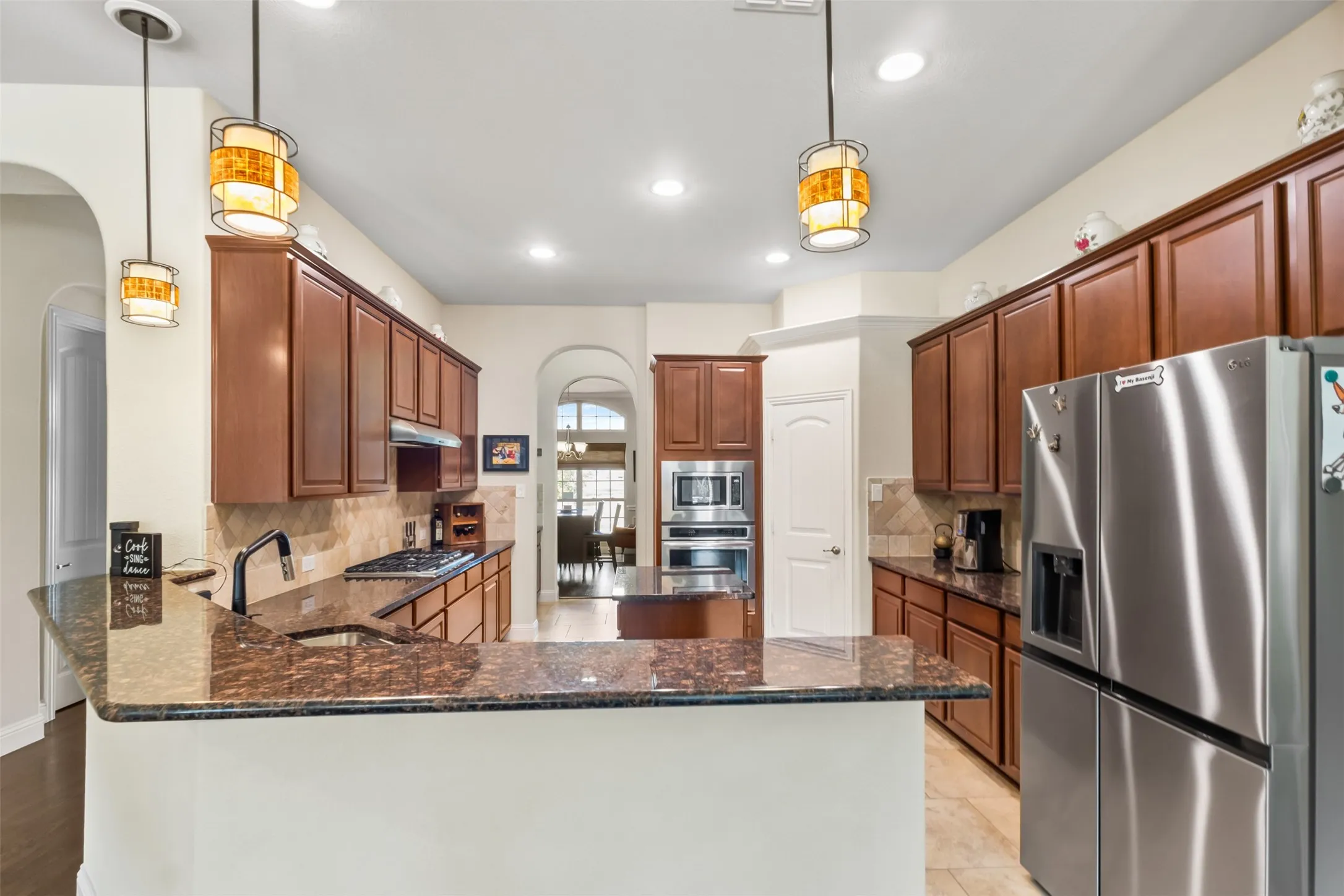 Kitchen featuring dark wood cabinetry, stainless steel appliances, speckled countertops, and a tile backsplash