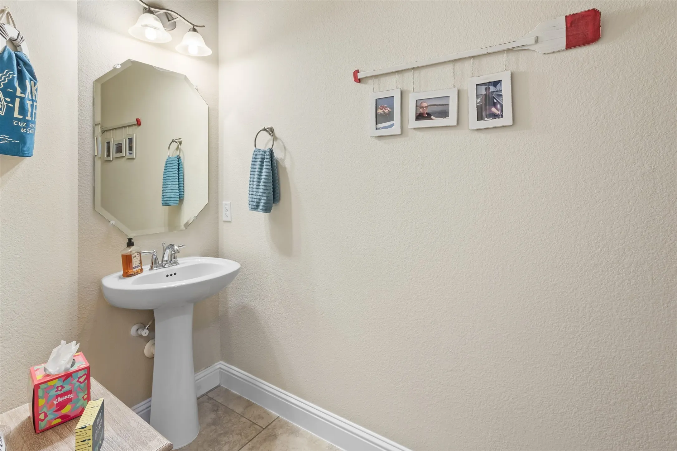 Pedestal sink with chrome faucet, octagonal mirror, and wall-mounted vanity lighting