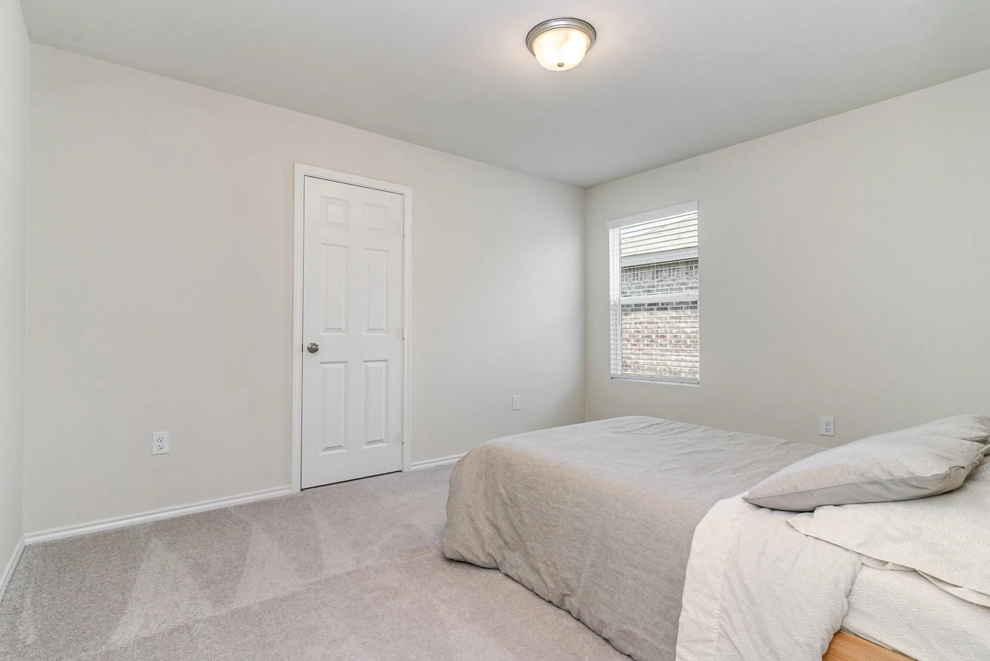 Light gray wall paint, white trim, gray carpet flooring, white paneled door, and a flush mount ceiling light fixture