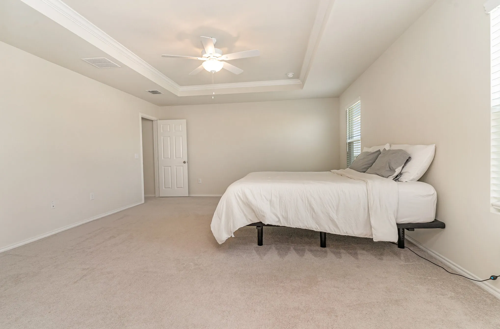 Tray ceiling with crown molding, ceiling fan, white paneled door, light wall paint, and carpet flooring