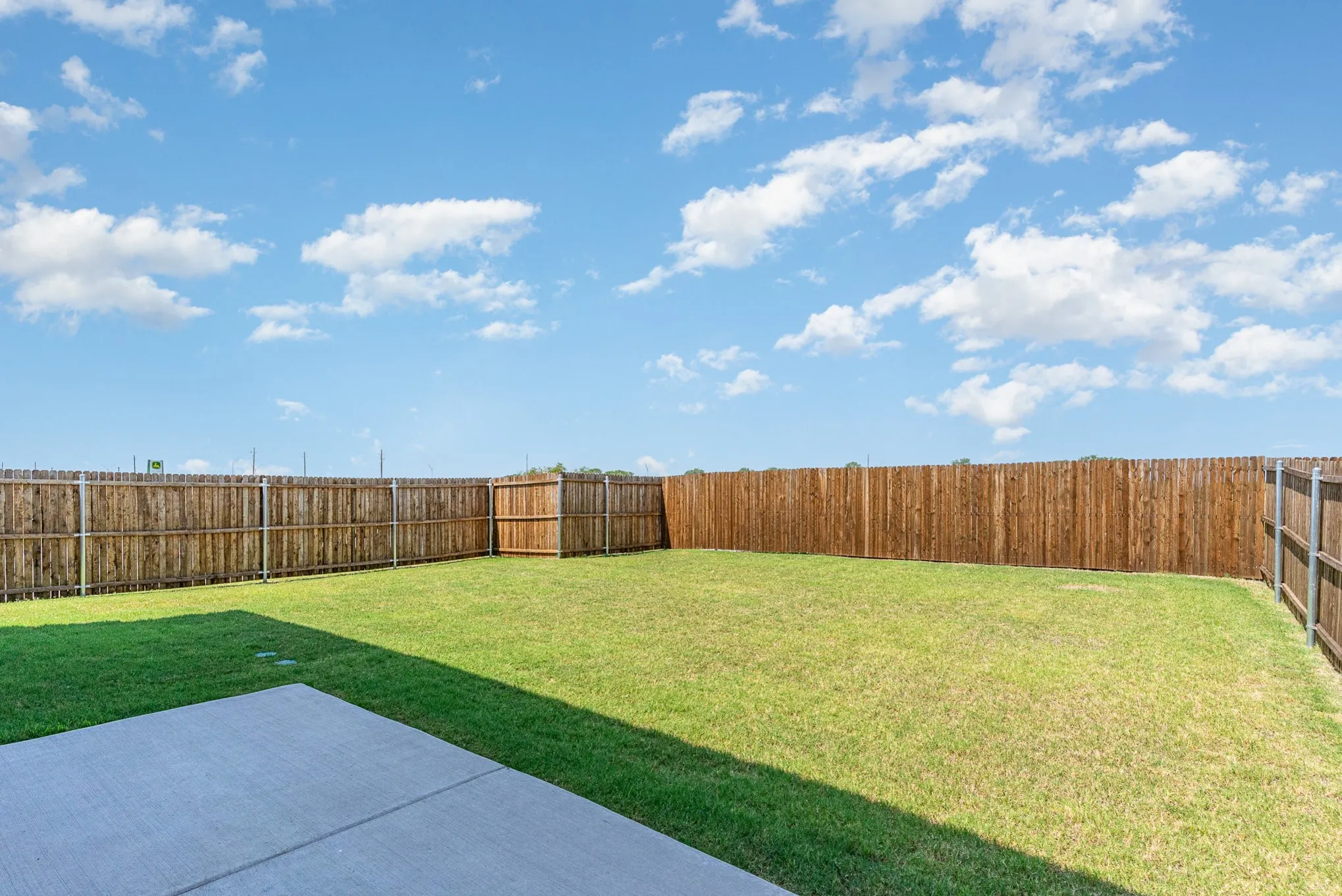 Expansive backyard featuring a manicured lawn, wood privacy fencing, and a concrete patio