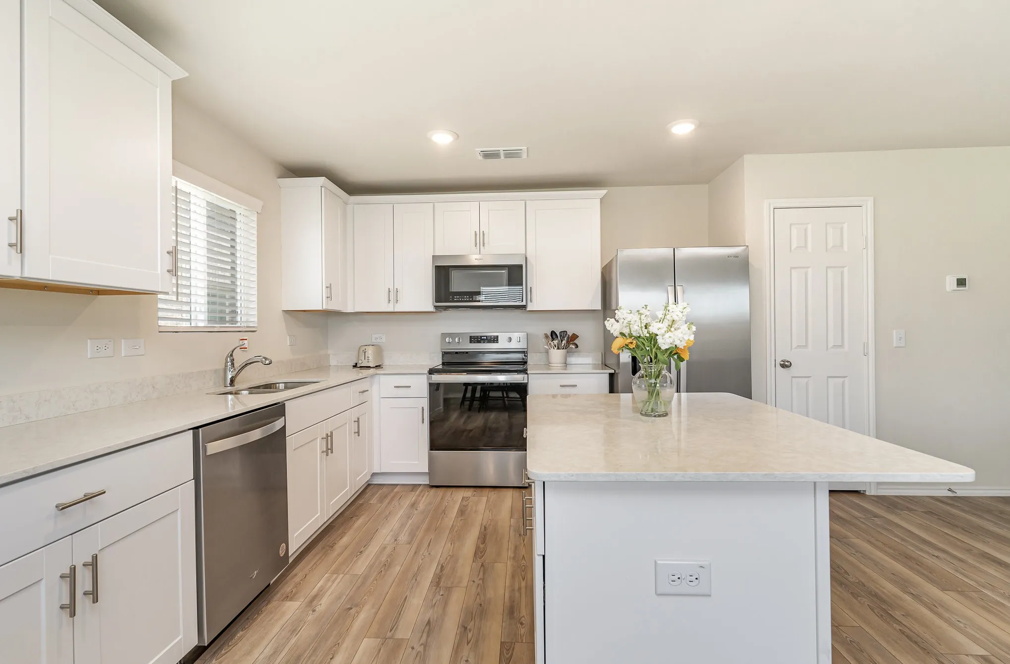 Kitchen featuring white cabinetry, light-toned countertops, stainless steel appliances, a kitchen island, and wood-finish flooring