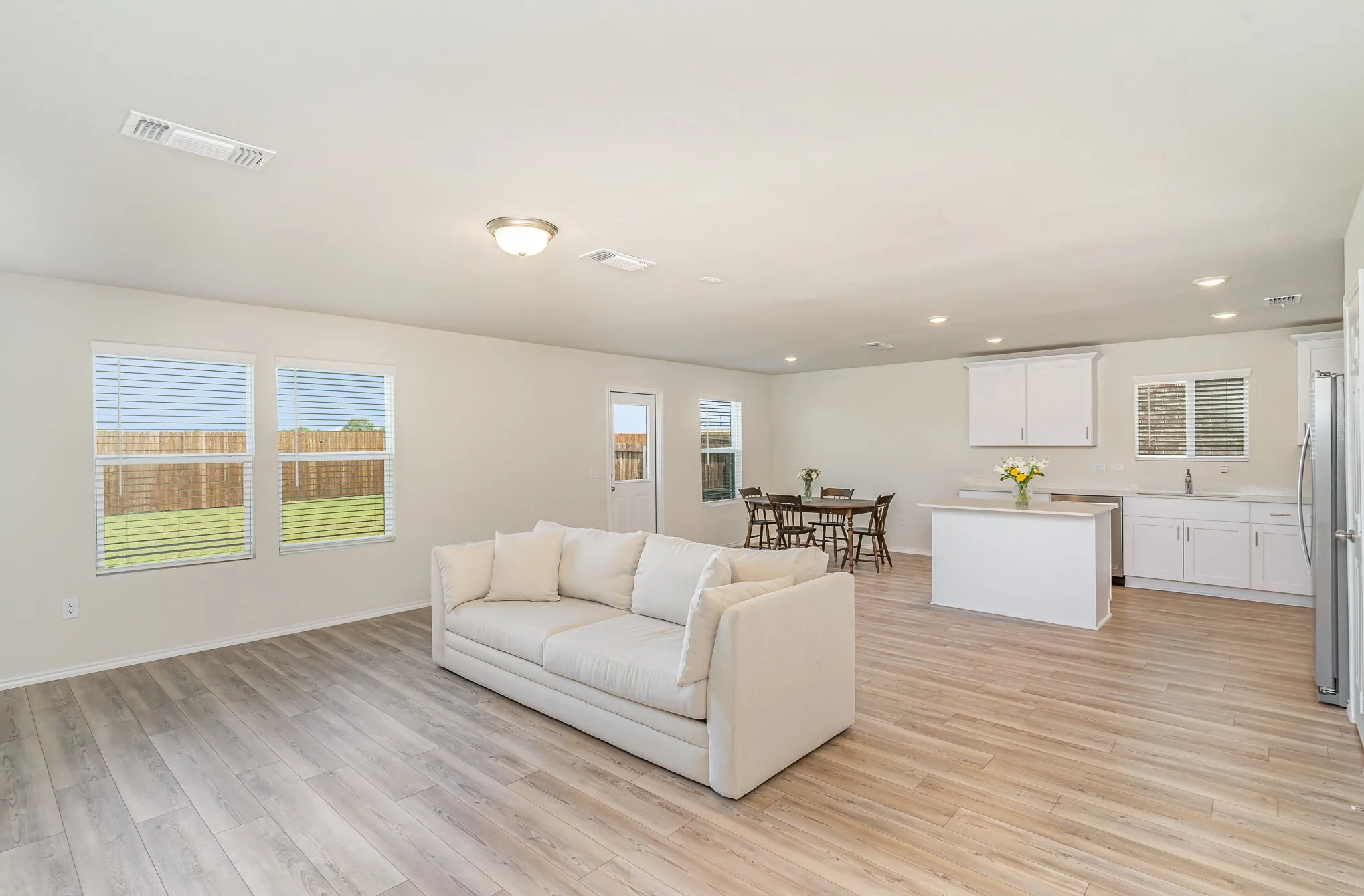 Open-concept living space with wood-finish flooring, multiple windows, recessed lighting, white kitchen cabinetry, and a kitchen island