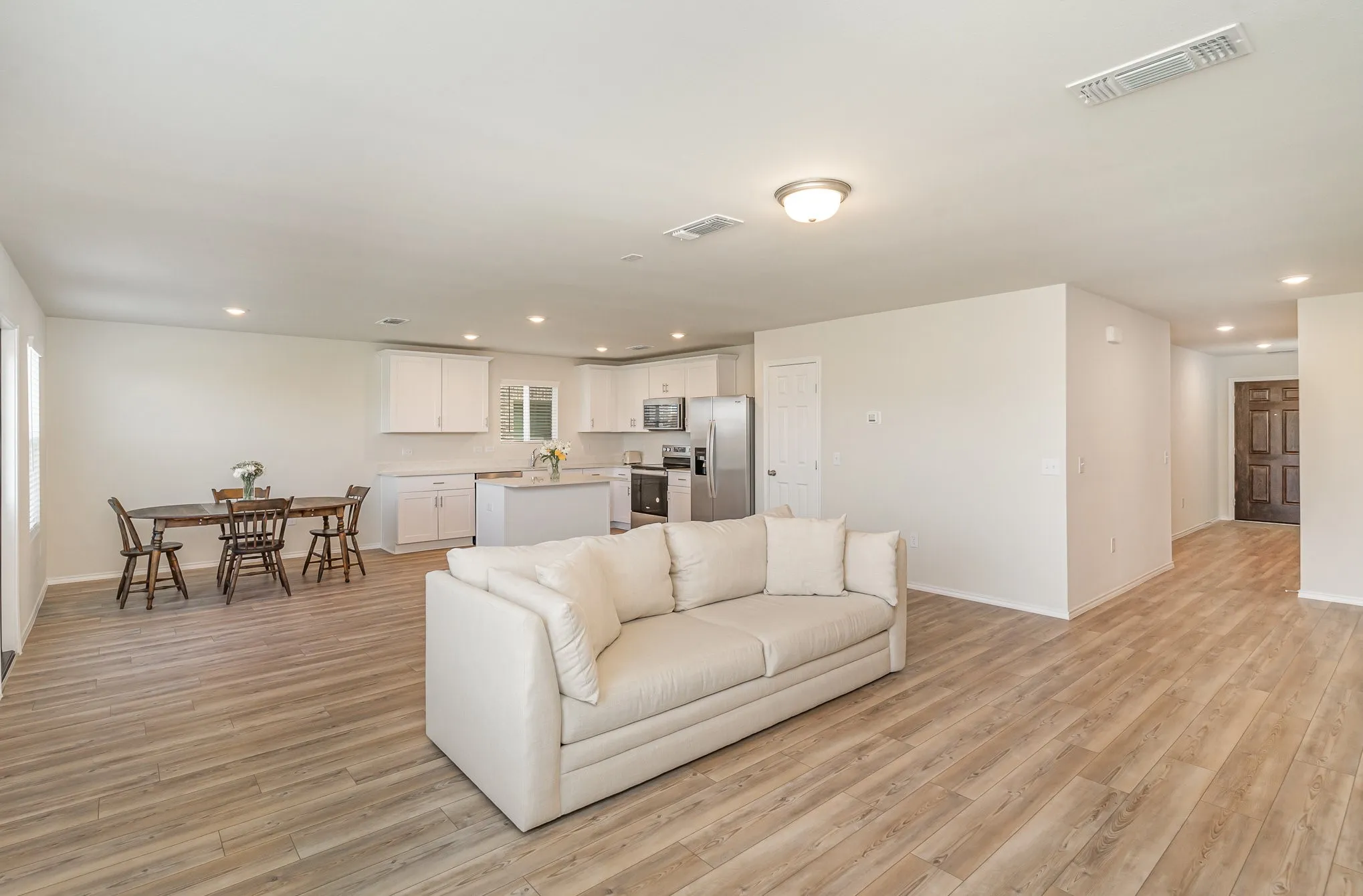 Open-concept living area featuring wood-finish flooring, recessed lighting, and a kitchen with white cabinetry and stainless steel appliances