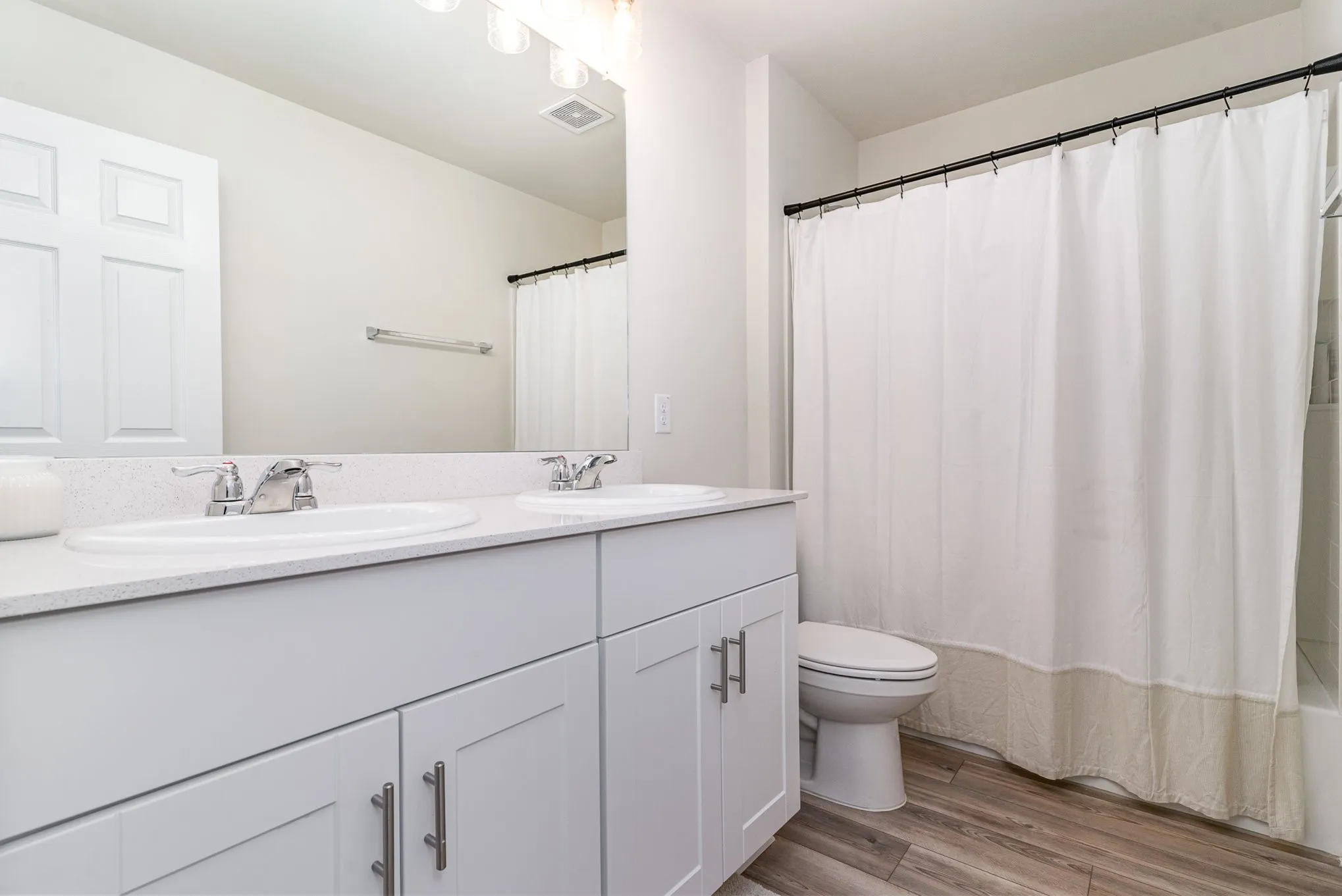 Double vanity with undermount sinks and chrome fixtures, white cabinetry, integrated countertop, and wood-finish flooring