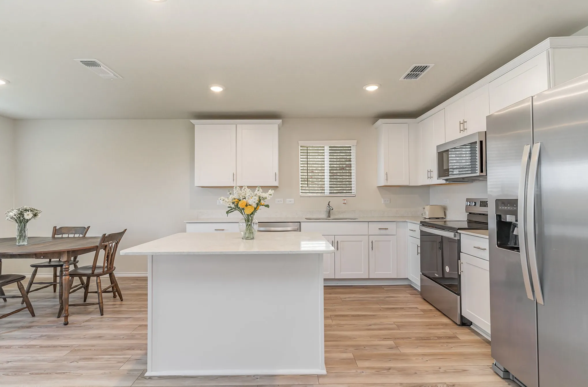 White kitchen cabinetry with stainless steel appliances, a center island, light-toned countertops, and wood-finish flooring