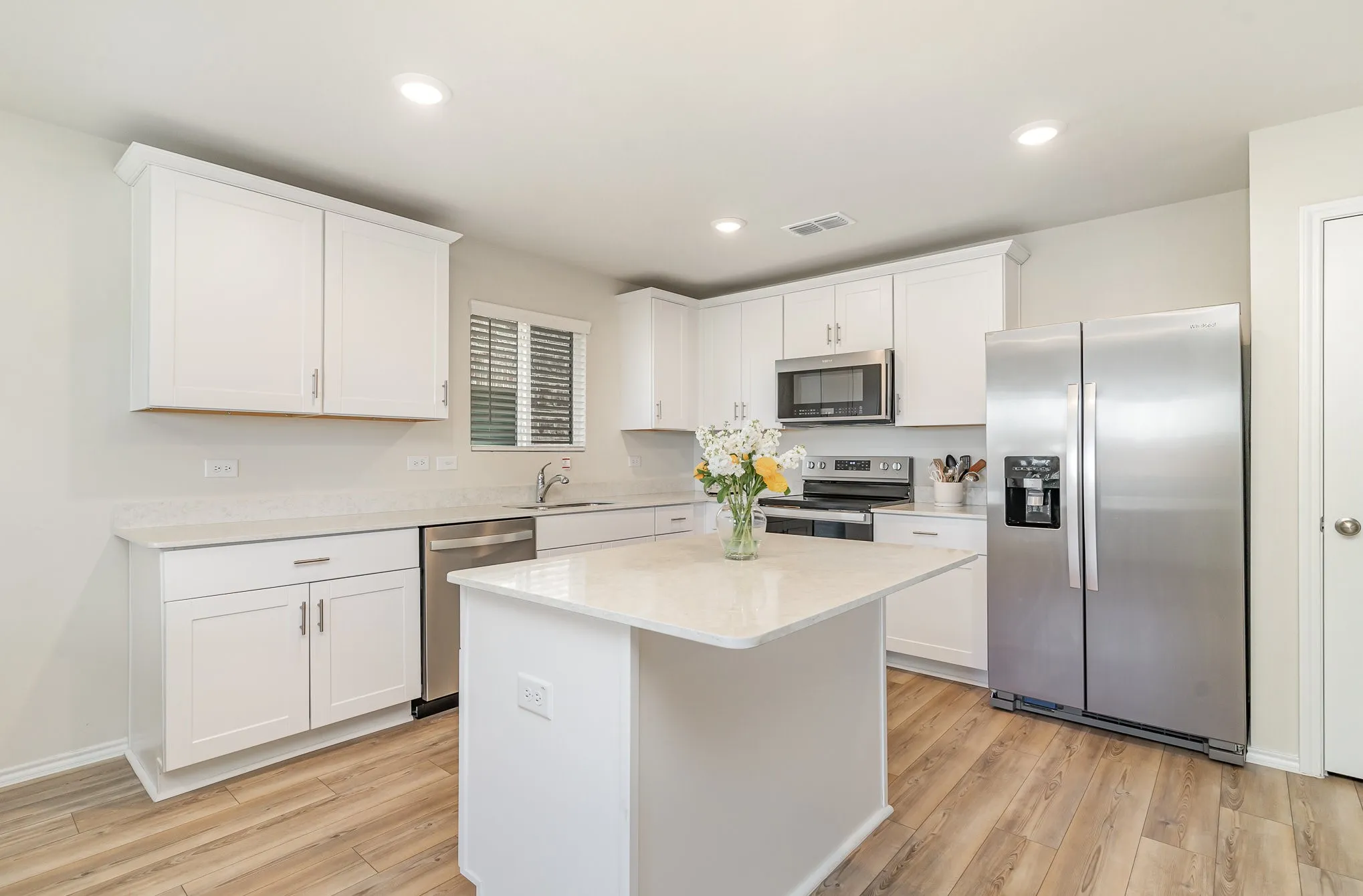 Kitchen featuring white cabinetry, light-toned countertops, stainless steel appliances, a center island, and wood-finish flooring