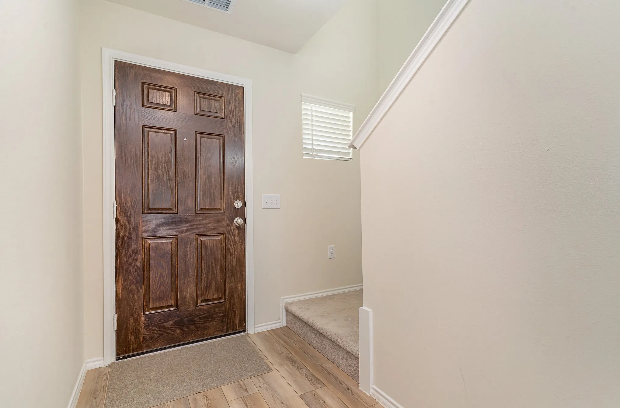 Six-panel entry door with a rich wood-grain finish, leading to wood-finish flooring