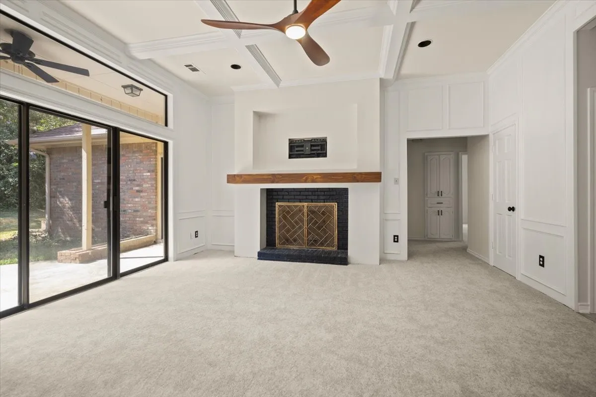 Coffered ceiling, wood-finish ceiling fan, fireplace with a wood mantle and brick surround, sliding glass doors, and carpeted flooring