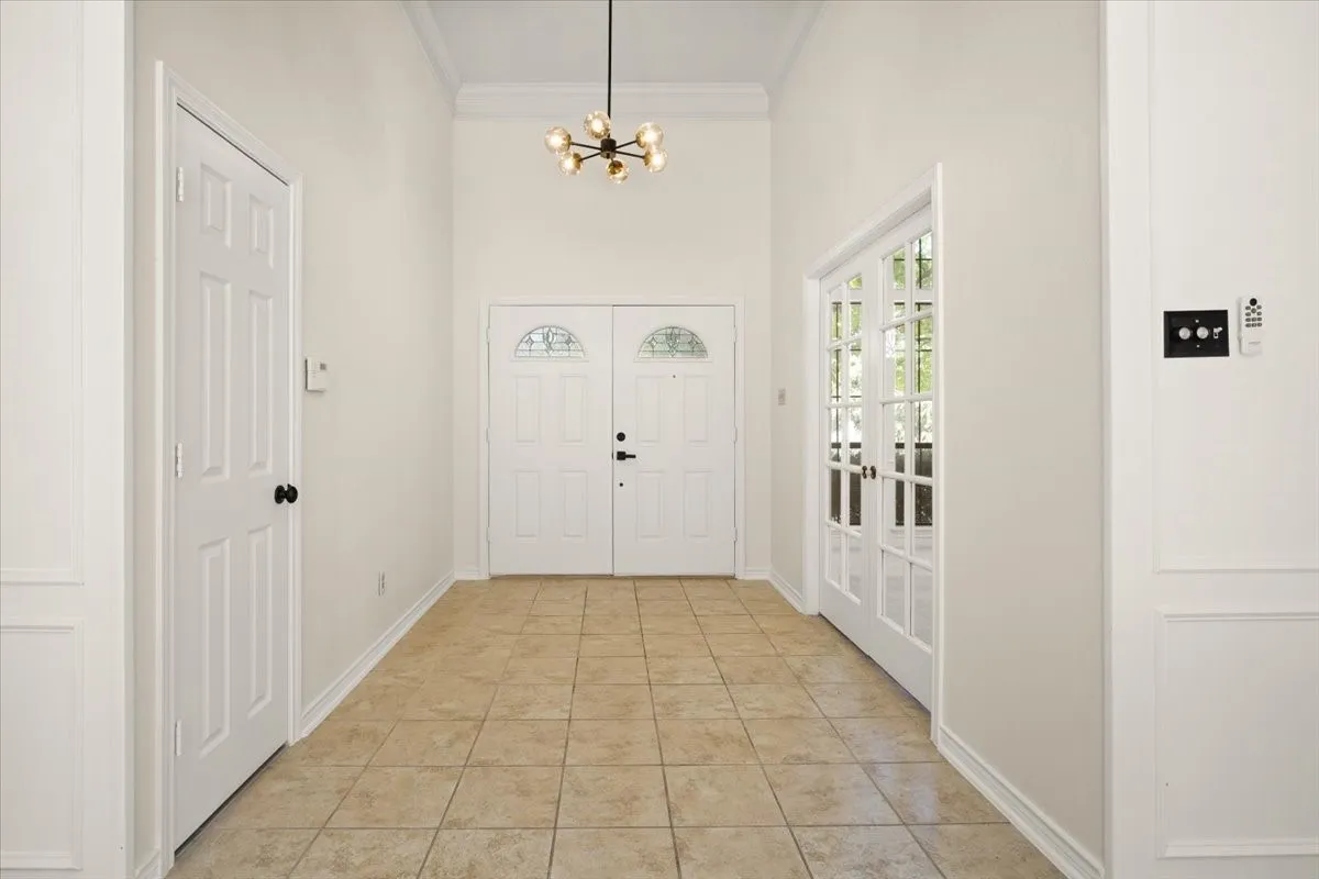 Tiled flooring, double entry doors with decorative glass inserts, modern chandelier, double French doors, and crown molding