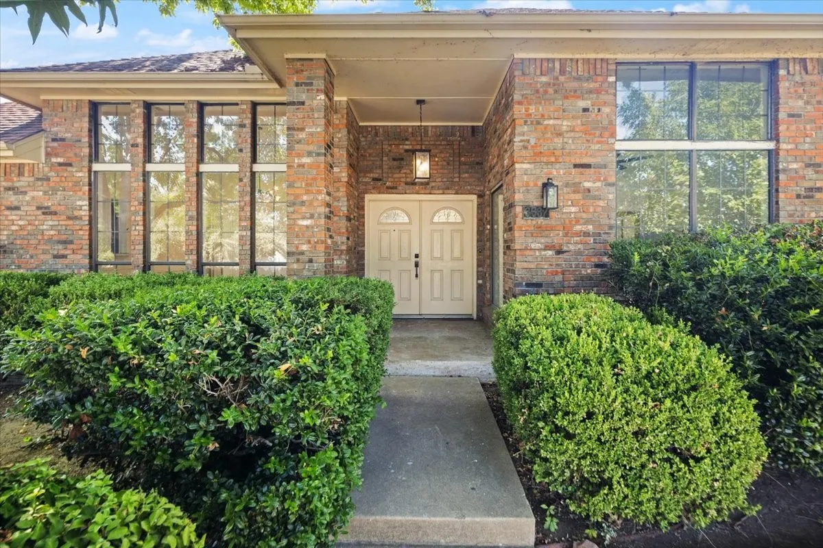 Brick exterior with a covered entry, double entry doors, large windows, and established shrubs