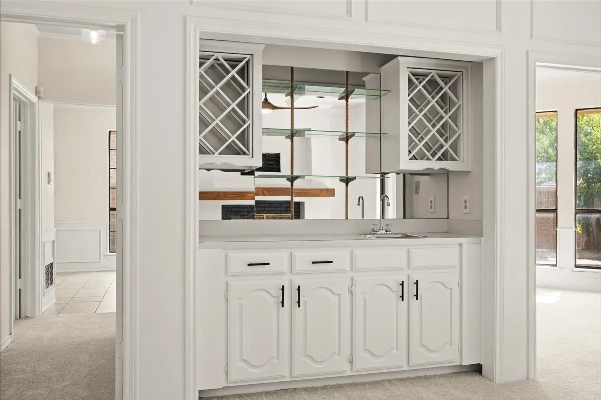Elegant wet bar featuring custom white cabinetry with paneled doors, dual undermount sinks, polished chrome hardware, and mirrored backsplash with geometric pattern glass-front upper cabinets