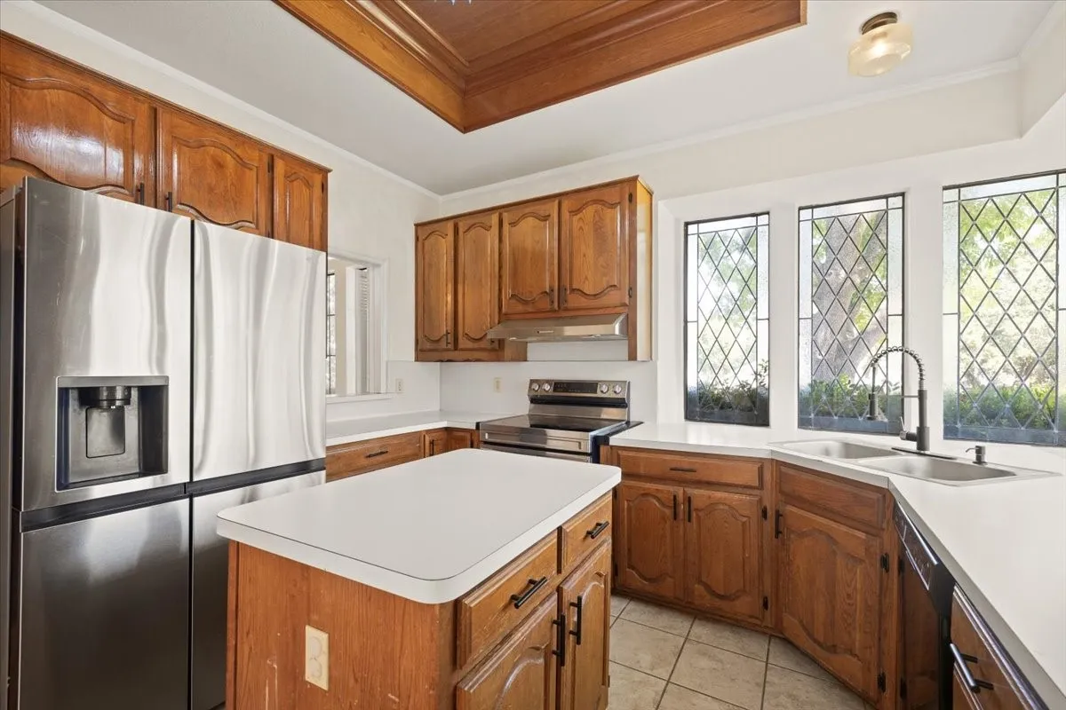 Kitchen featuring wood cabinetry, white countertops, a central island, stainless steel refrigerator, and leaded glass windows