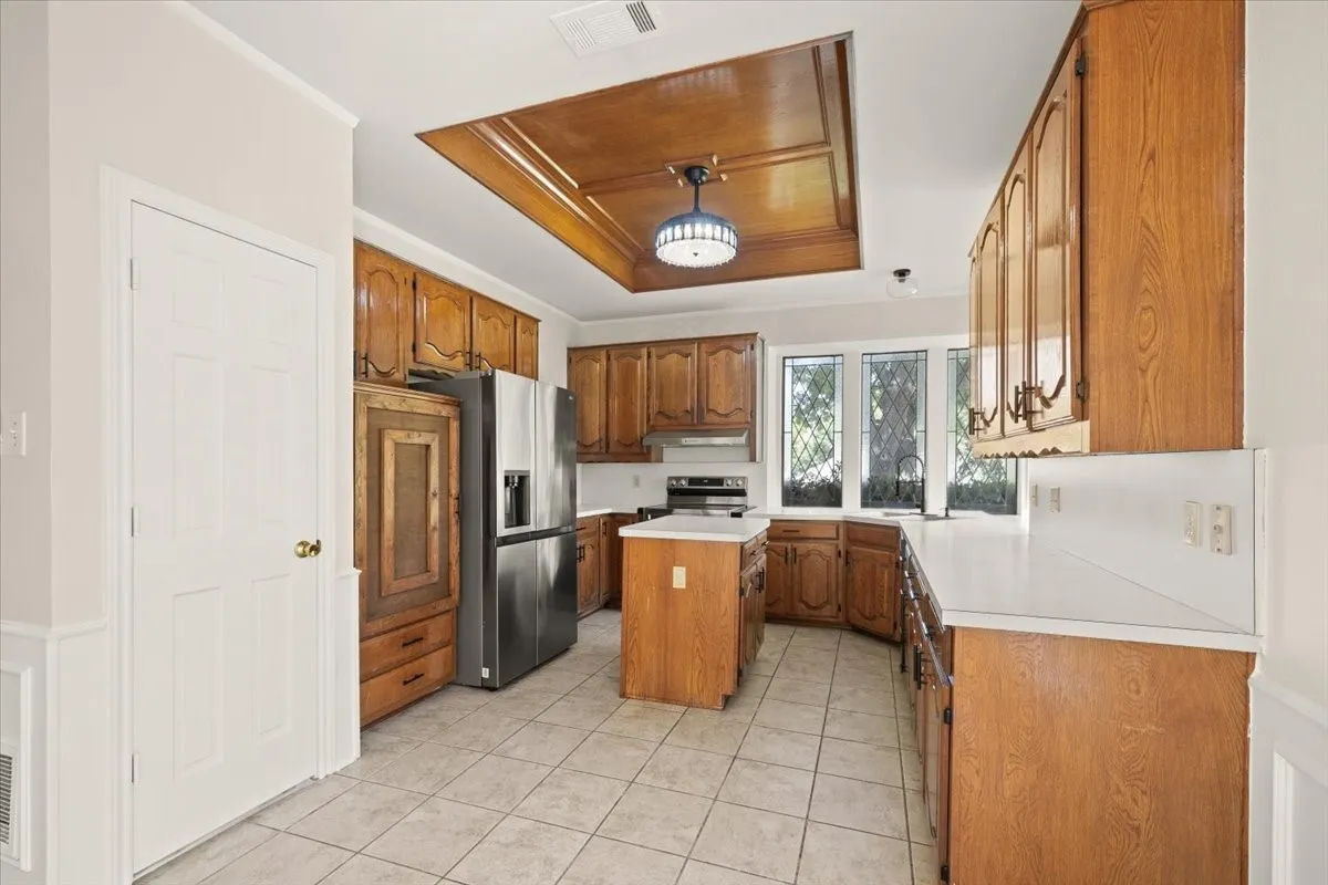 Kitchen with wood cabinetry, light-toned countertops, a central island, tiled flooring, and a coffered wood-paneled ceiling