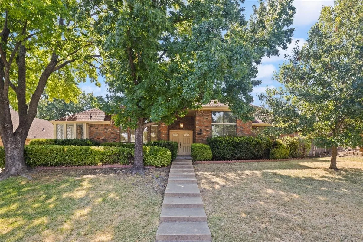 Brick exterior with a gabled roofline, mature trees, and established shrubbery