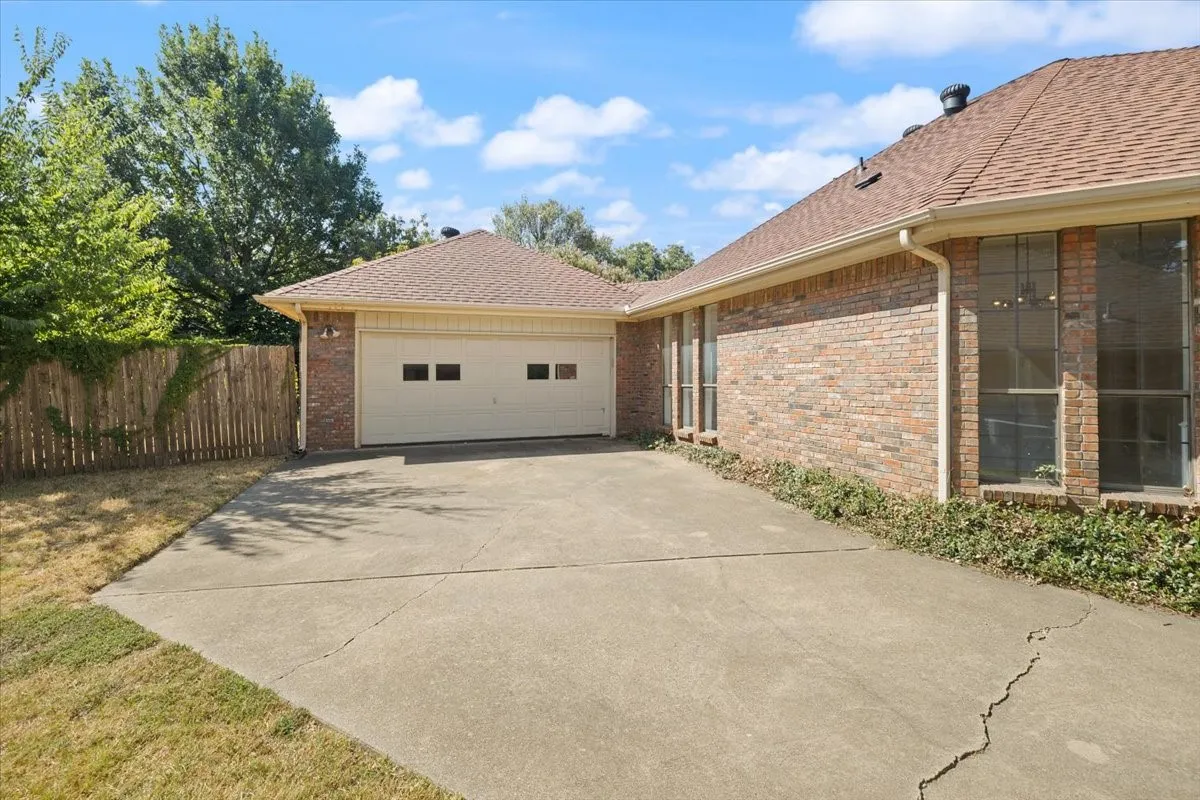 Two-car garage with an attached brick exterior home featuring large windows, a shingle roof, and a concrete driveway
